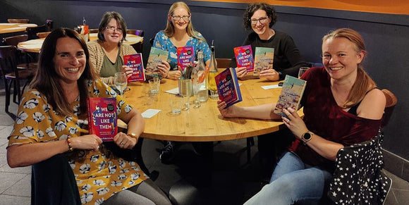 Women sit round table holding up books chosen for the first book club meeting. 