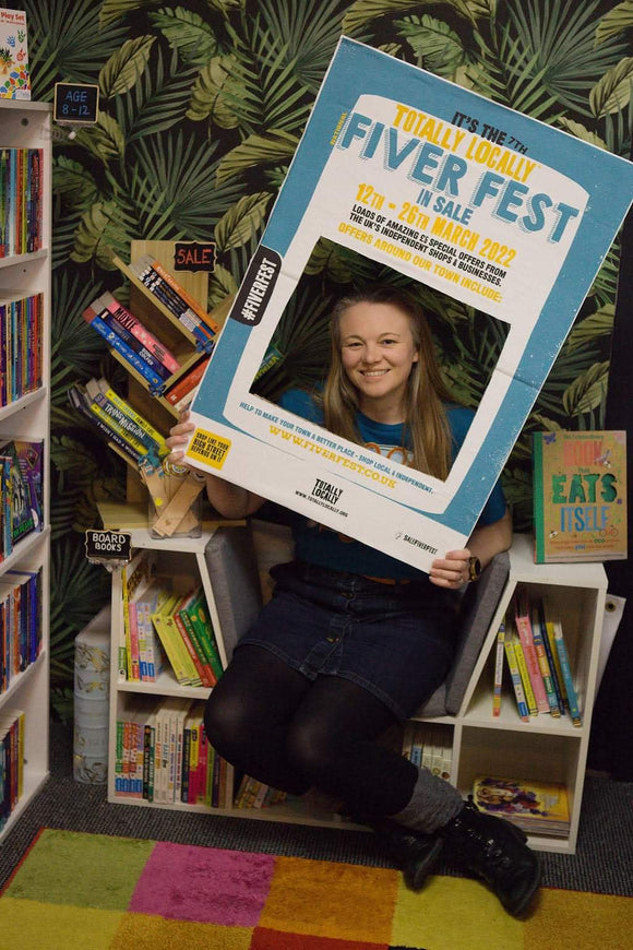 Owner of B For Butterfly Books, Michelle holding a photo frame board advertising Fiver Fest. 